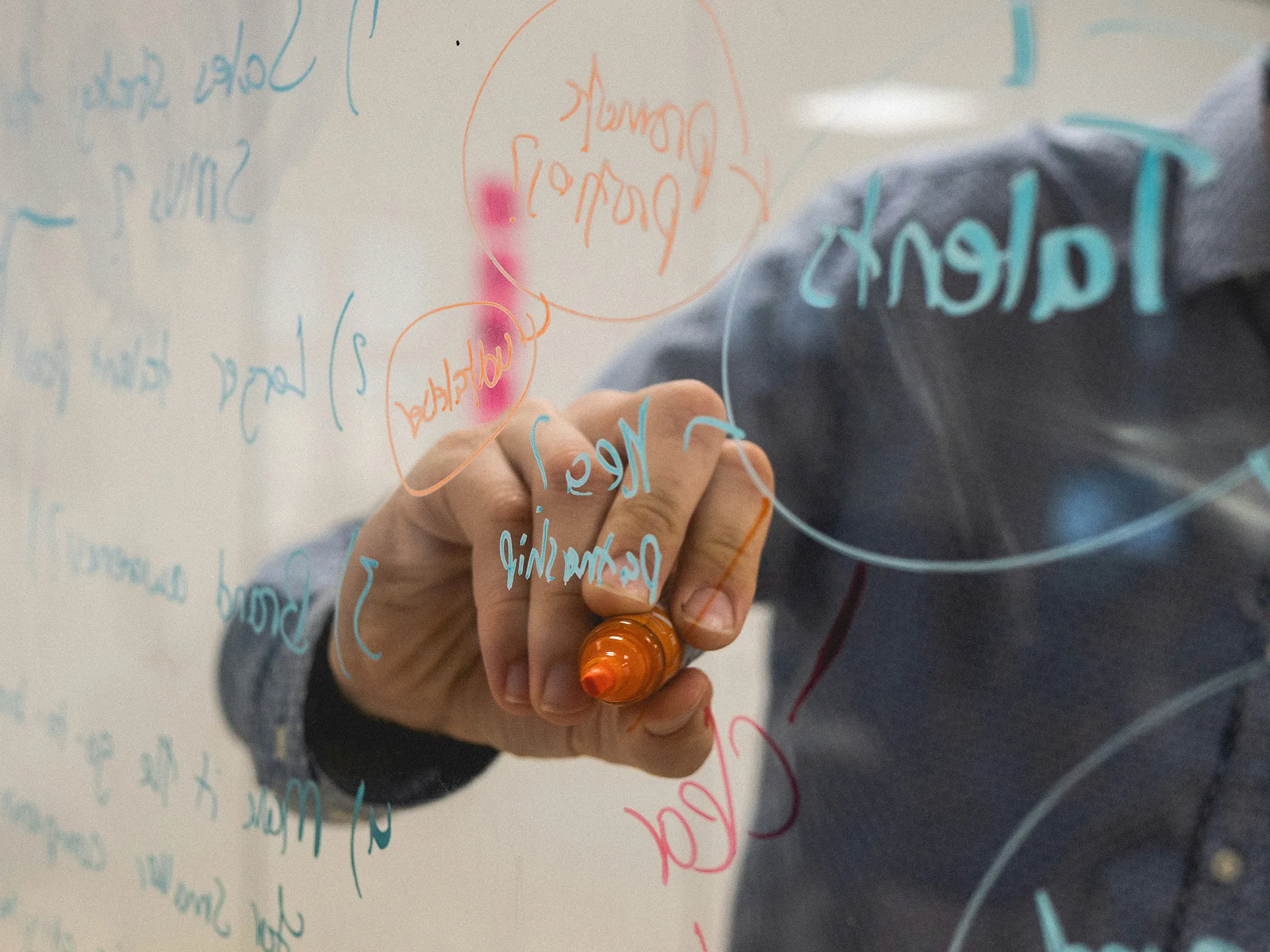 A man's hand holding a marker and writing on a transparent whiteboard