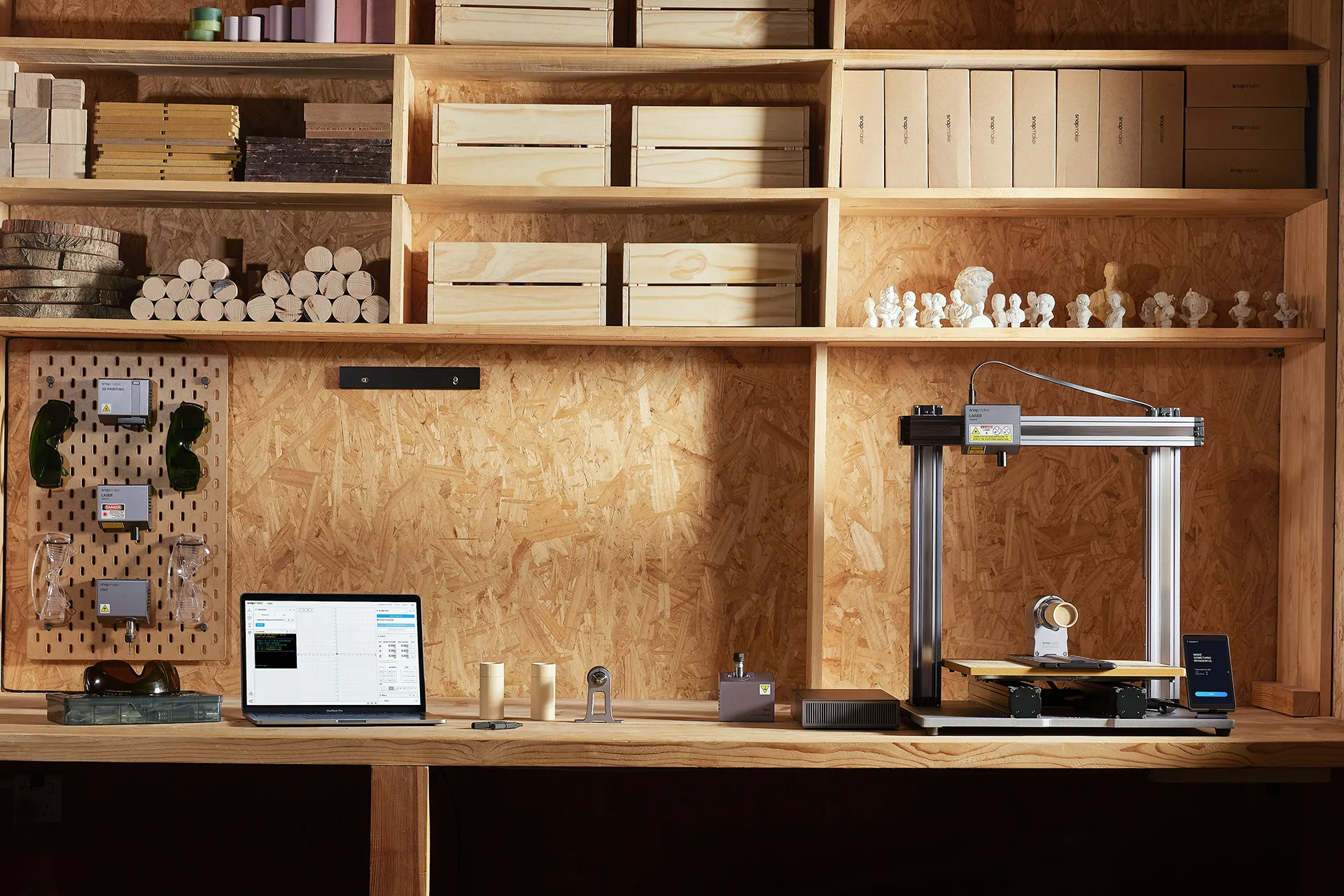 A computer resting on a wooden desk, with various work tools placed on it, and above it, there are wooden shelves holding various objects