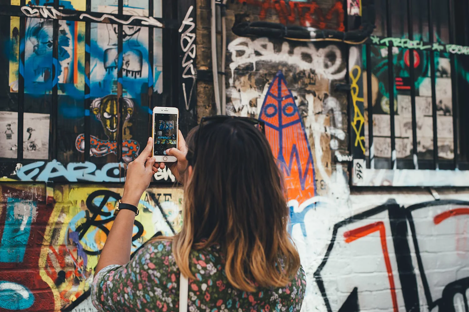 A woman from behind taking photos of murals with her cellphone.