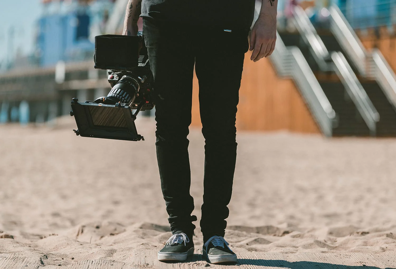 A person standing, of whom we see only one half, holding a professional camera in their right hand.