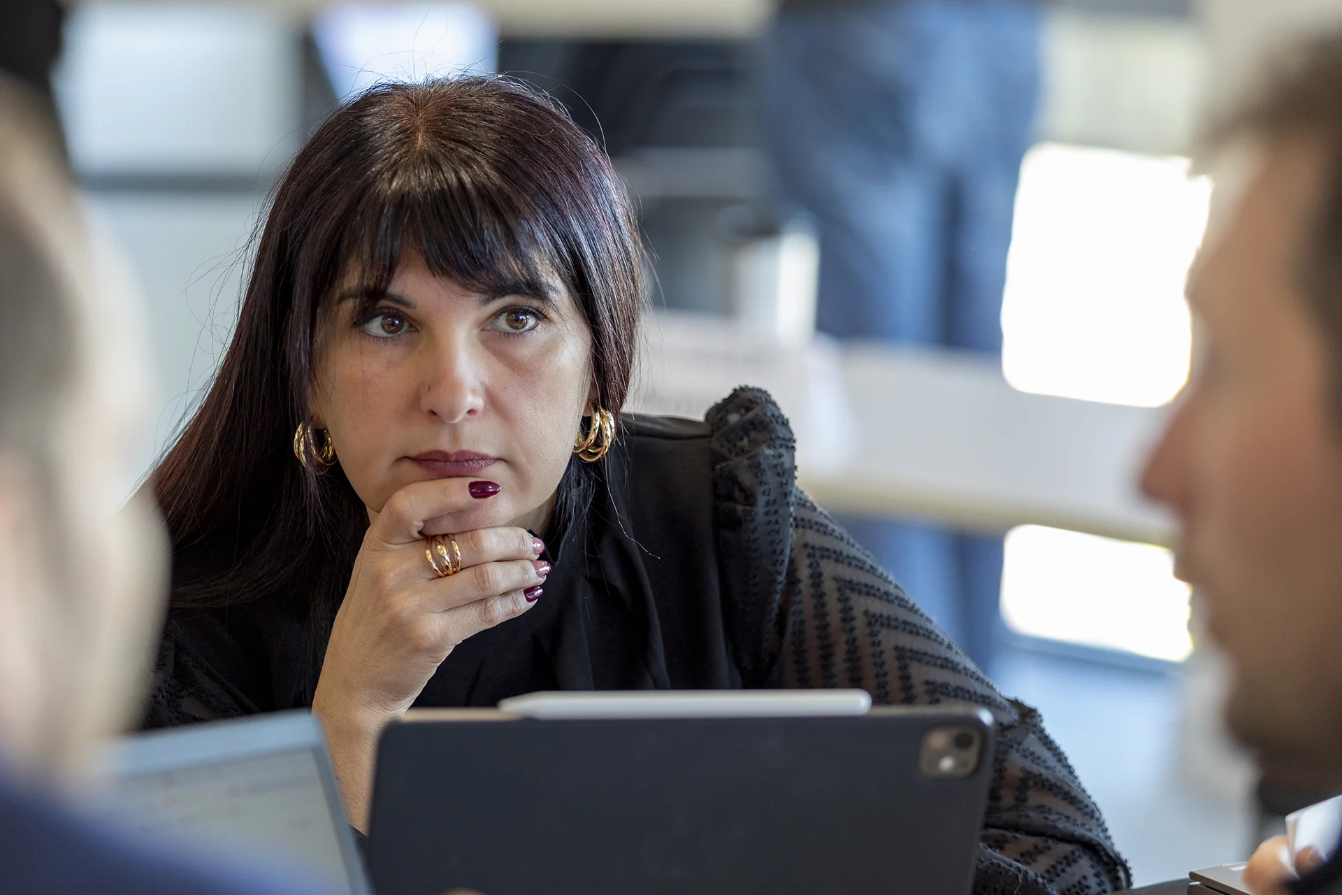 Groupe de collègues en réunion, avec un homme au centre tenant une tablette, tous semblent concentrés et engagés dans una discussion collaborative