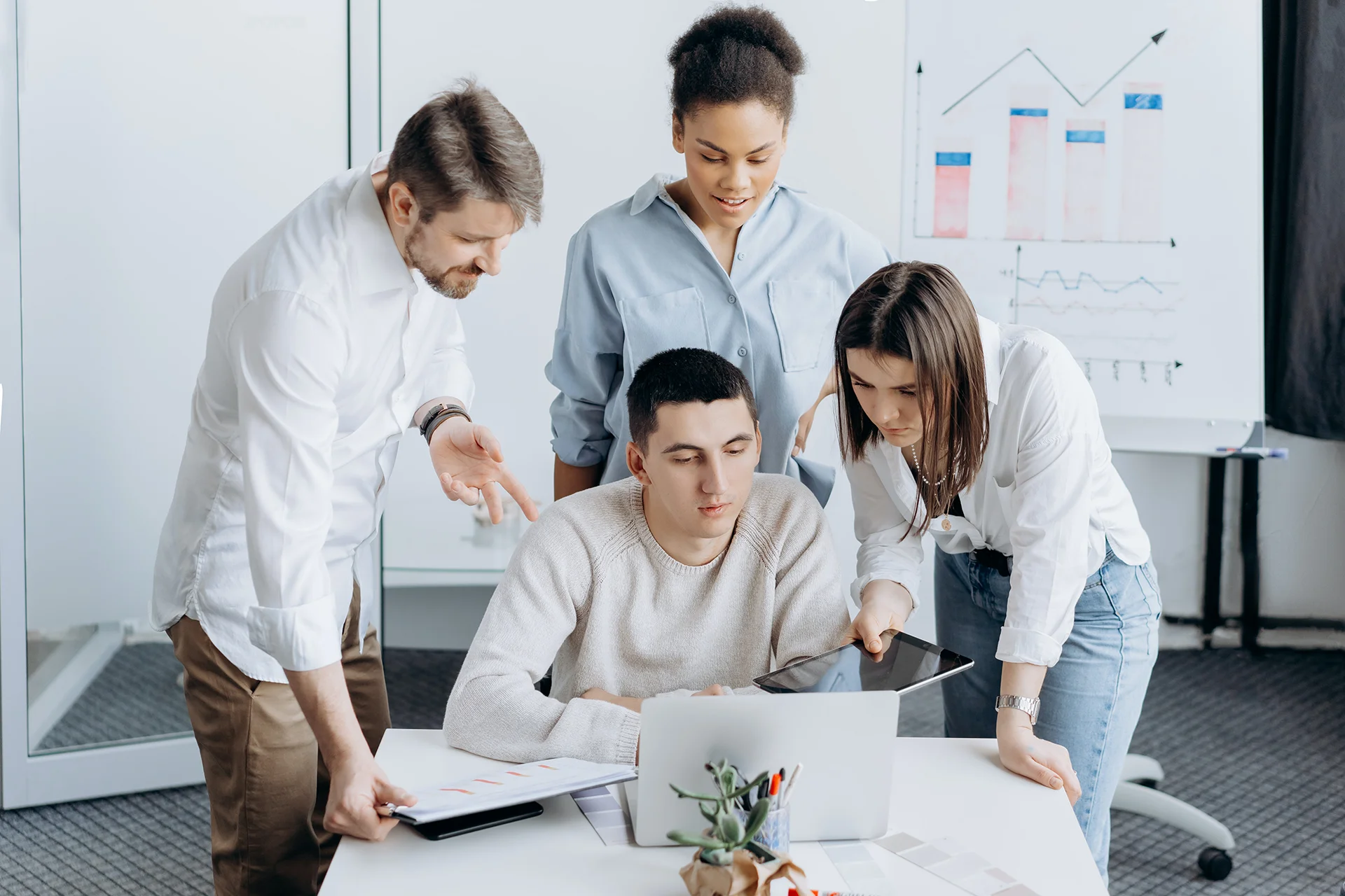 Groupe d’apprenants travaillant en équipe autour d’un ordinateur portable, analysant des documents et des graphiques dans une salle de formation.