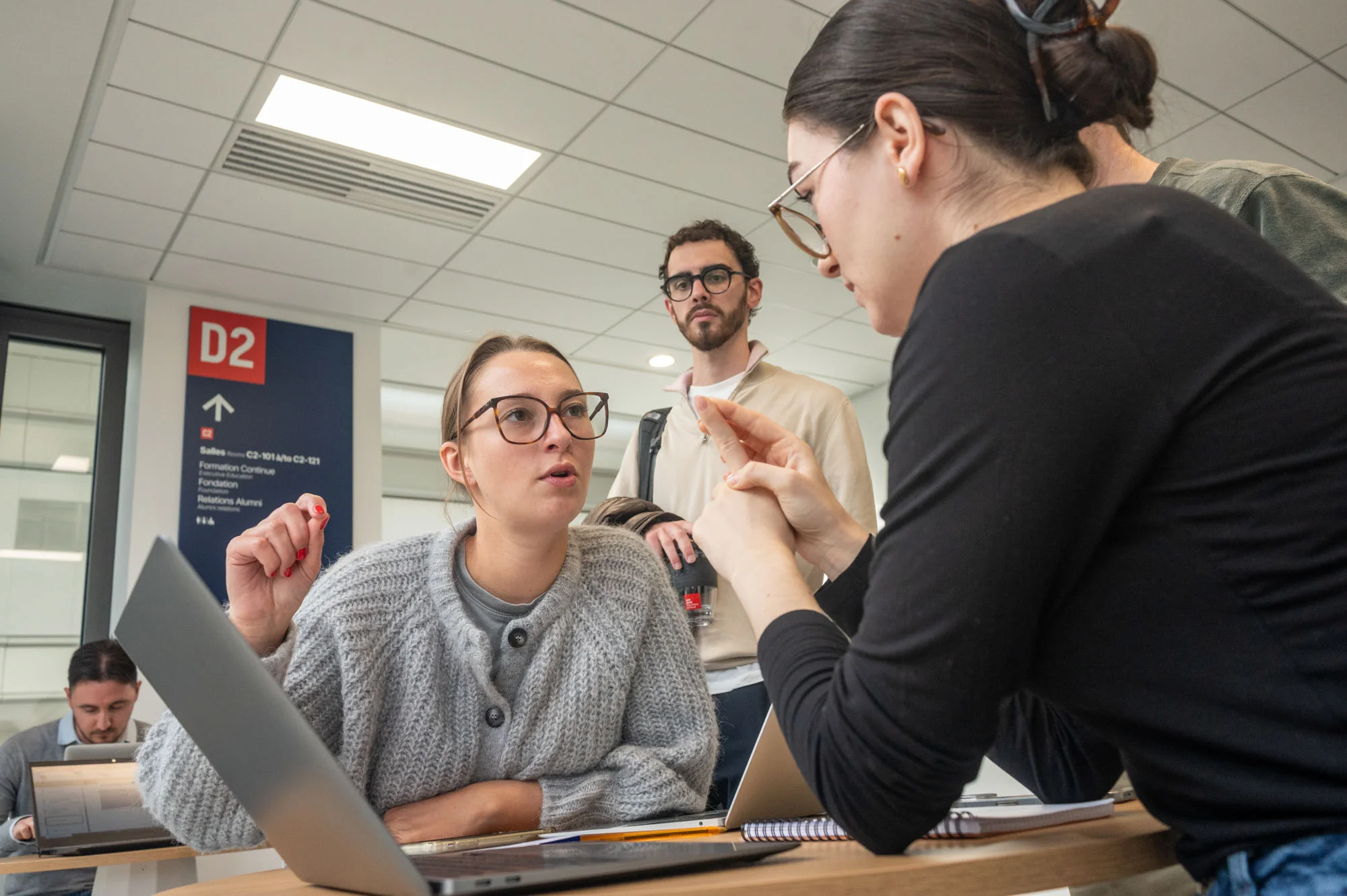Groupe de personnes travaillant ensemble autour d’une table avec des ordinateurs portables dans un espace intérieur lumineux, en échangeant des informations et des documents.