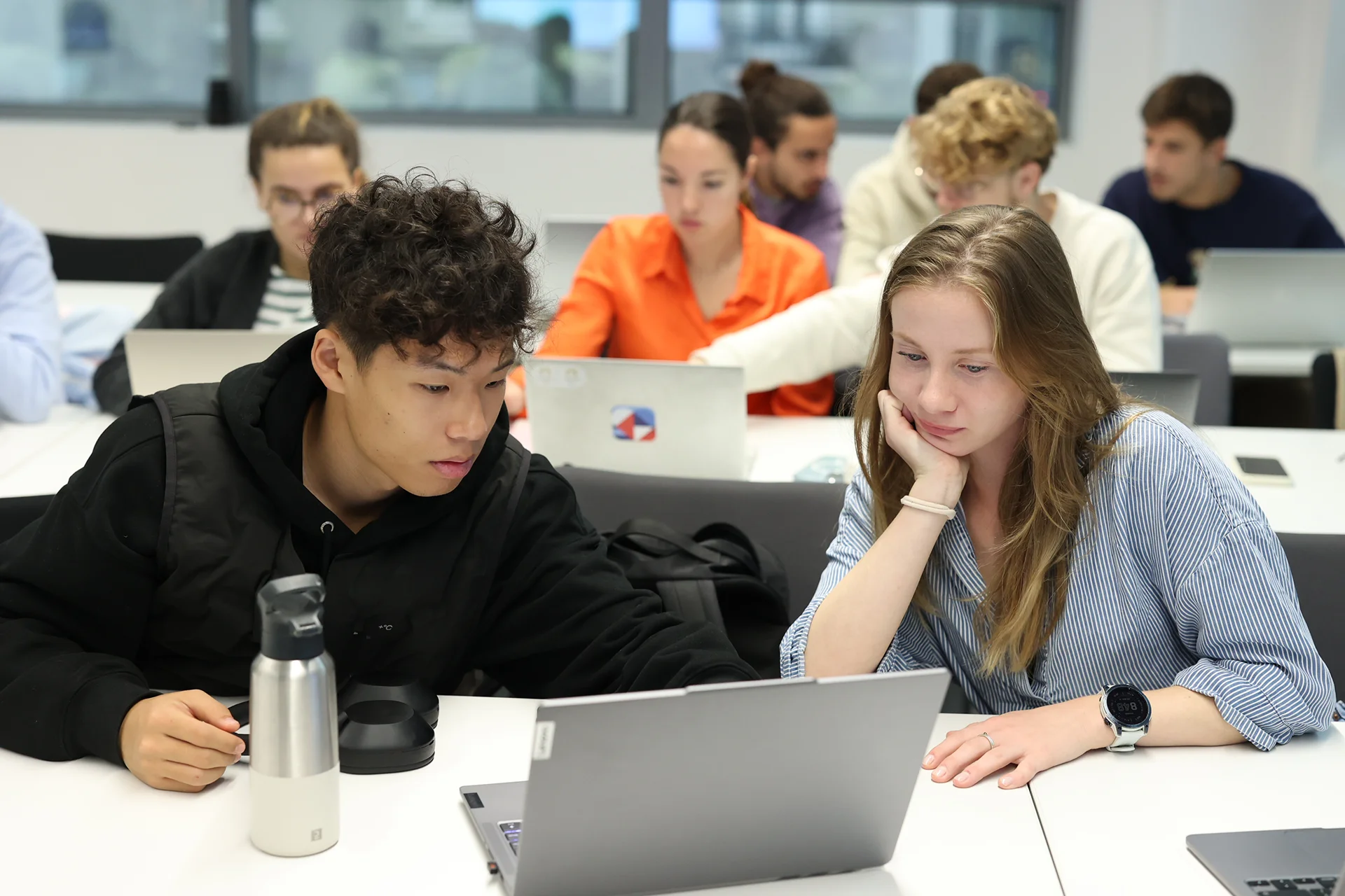 Étudiants travaillant ensemble sur un ordinateur portable dans une salle de classe moderne durant une session académique.