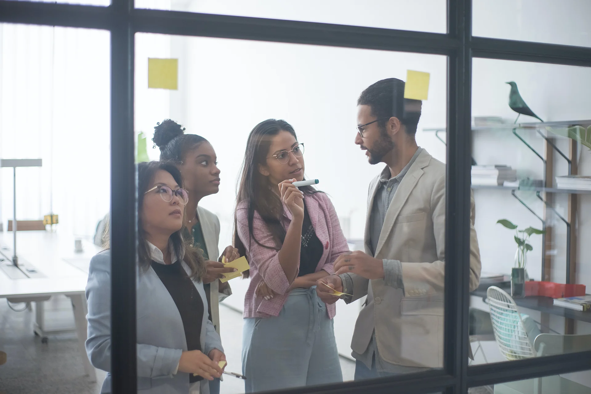 Team collaborating around a glass board, sharing ideas and working with sticky notes in a modern office workspace.