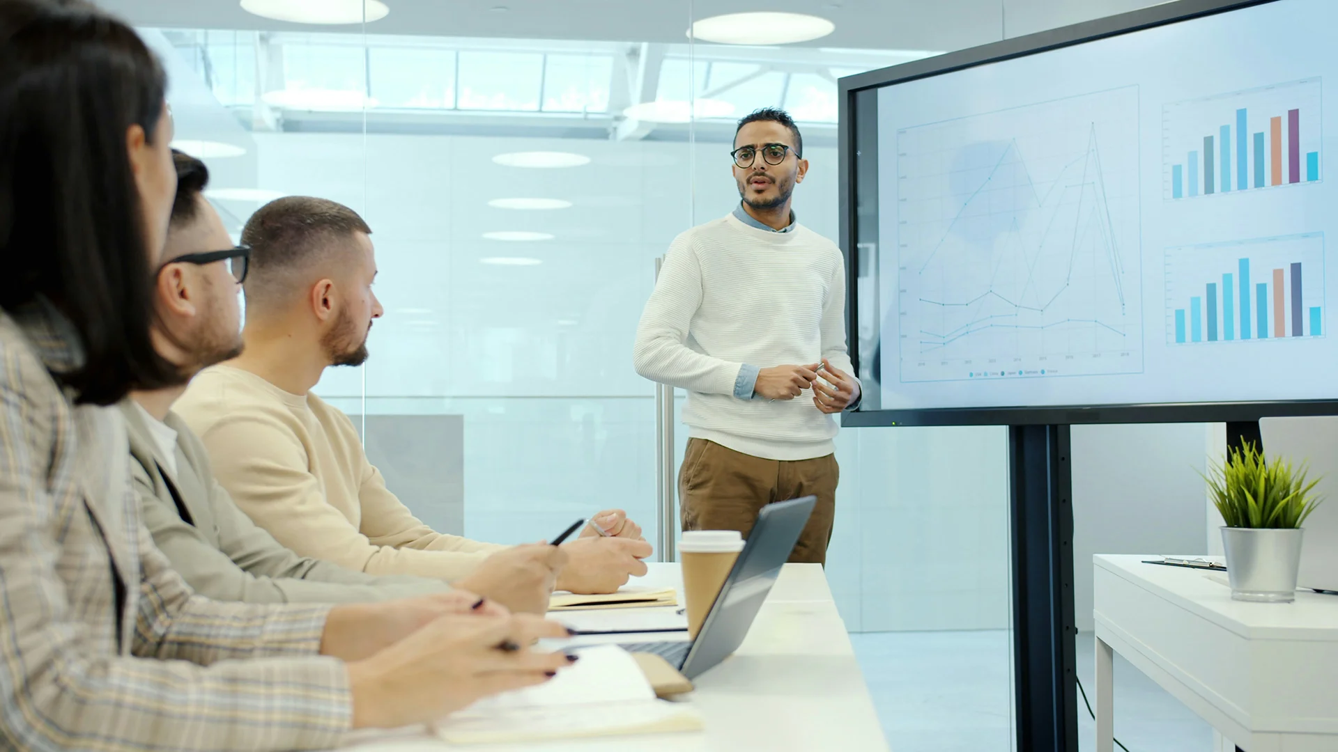Présentation professionnelle avec un intervenant expliquant des graphiques de performance à une équipe en réunion dans une salle de conférence moderne.
