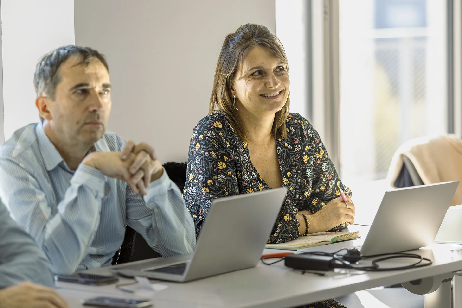 emlyon participants attending a training session, seated at a table with laptops, taking notes and working in a bright classroom setting.