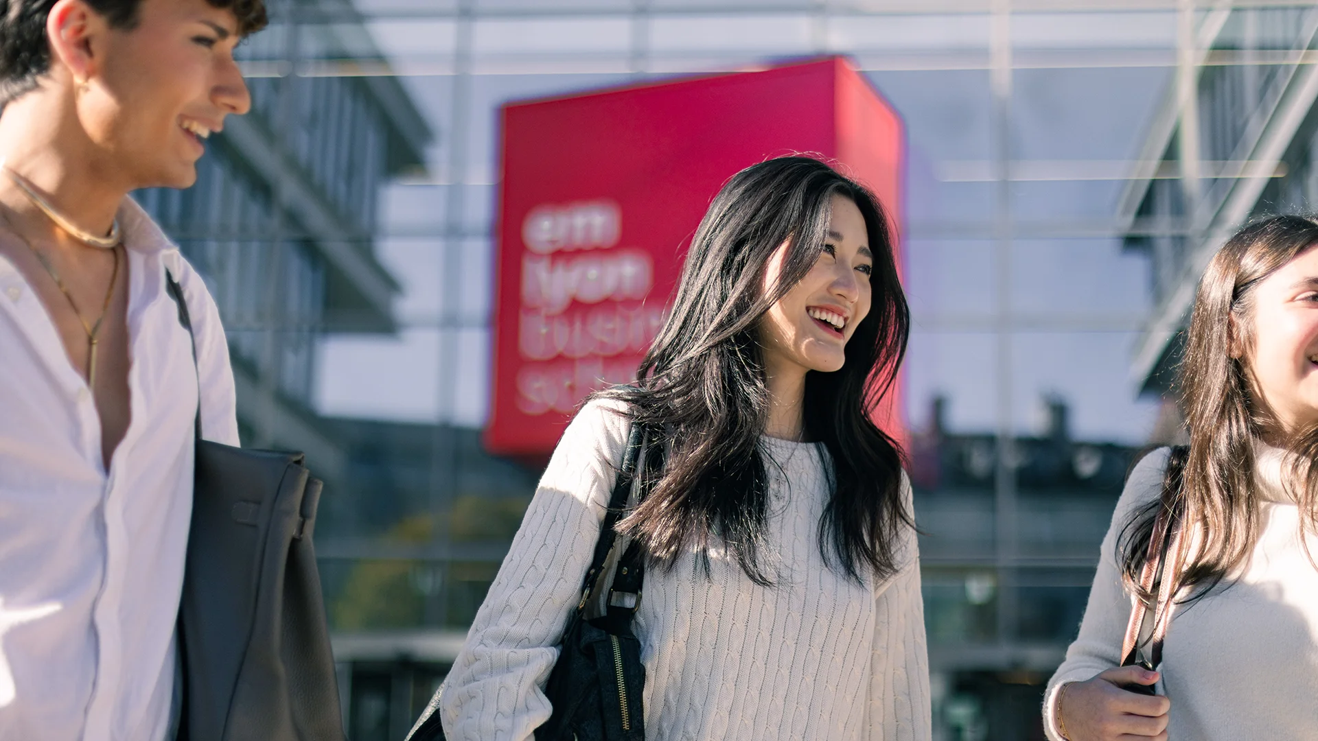 Étudiantes et étudiants d’emlyon business school se déplaçant à l’extérieur du campus de Lyon, devant un bâtiment moderne et vitré.
