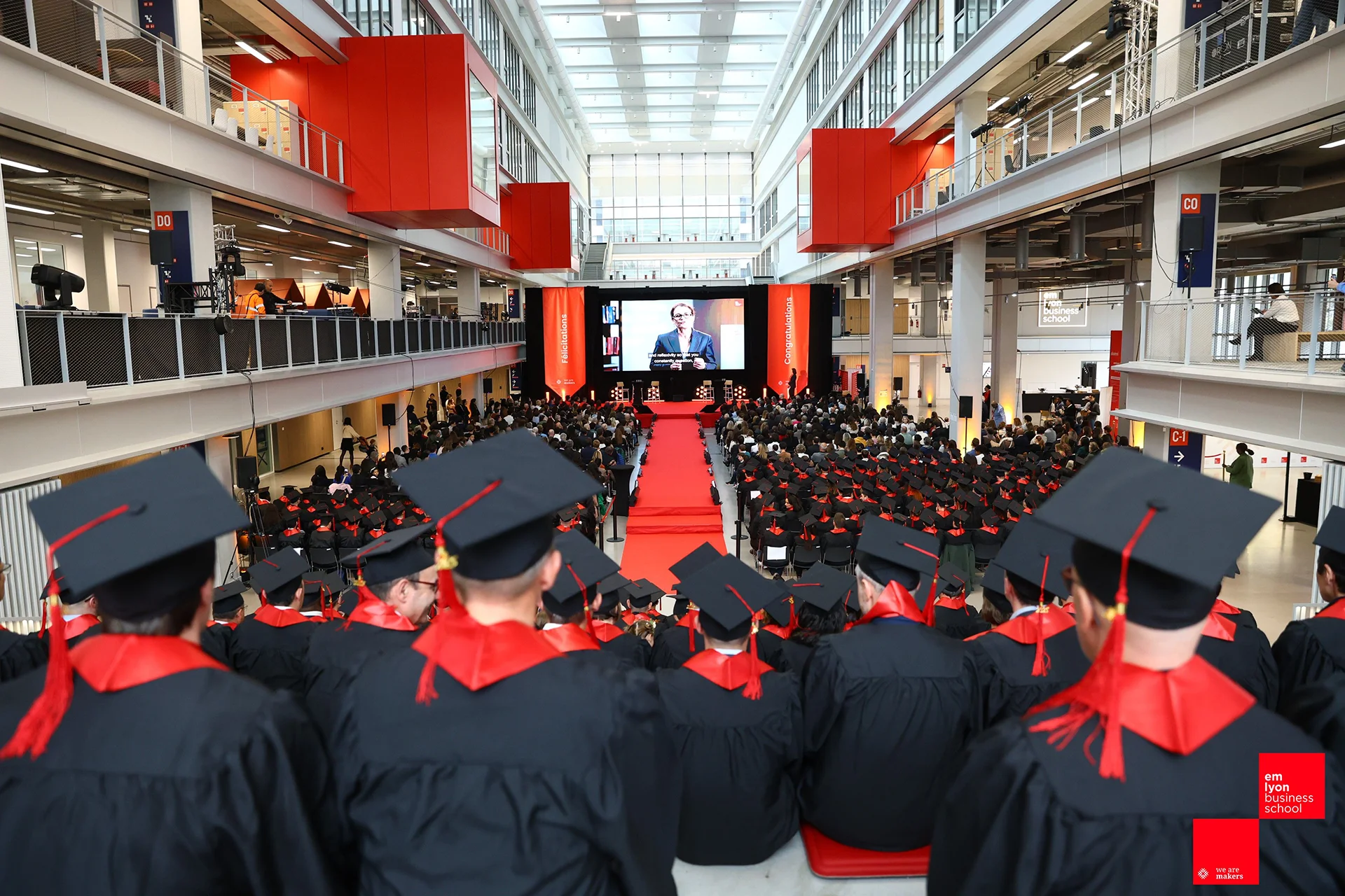 Wide view of the emlyon business school graduation ceremony in the atrium, with graduates seated facing the stage.
