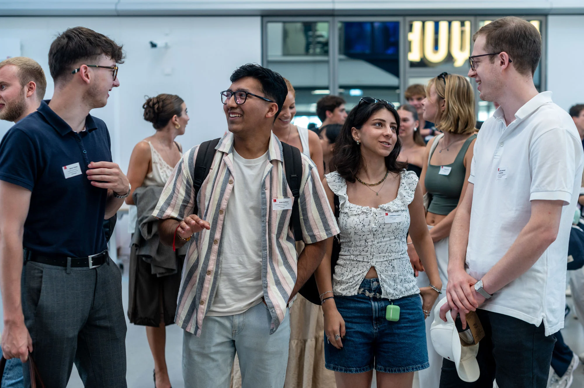 Group of people wearing name badges walking and conversing inside the emlyon campus in Lyon during a student event.