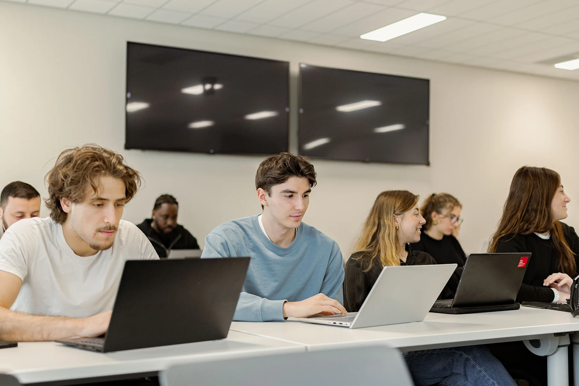 Executive MBA participants attending a class at emlyon, seated at desks and working on laptops in a modern learning environment.