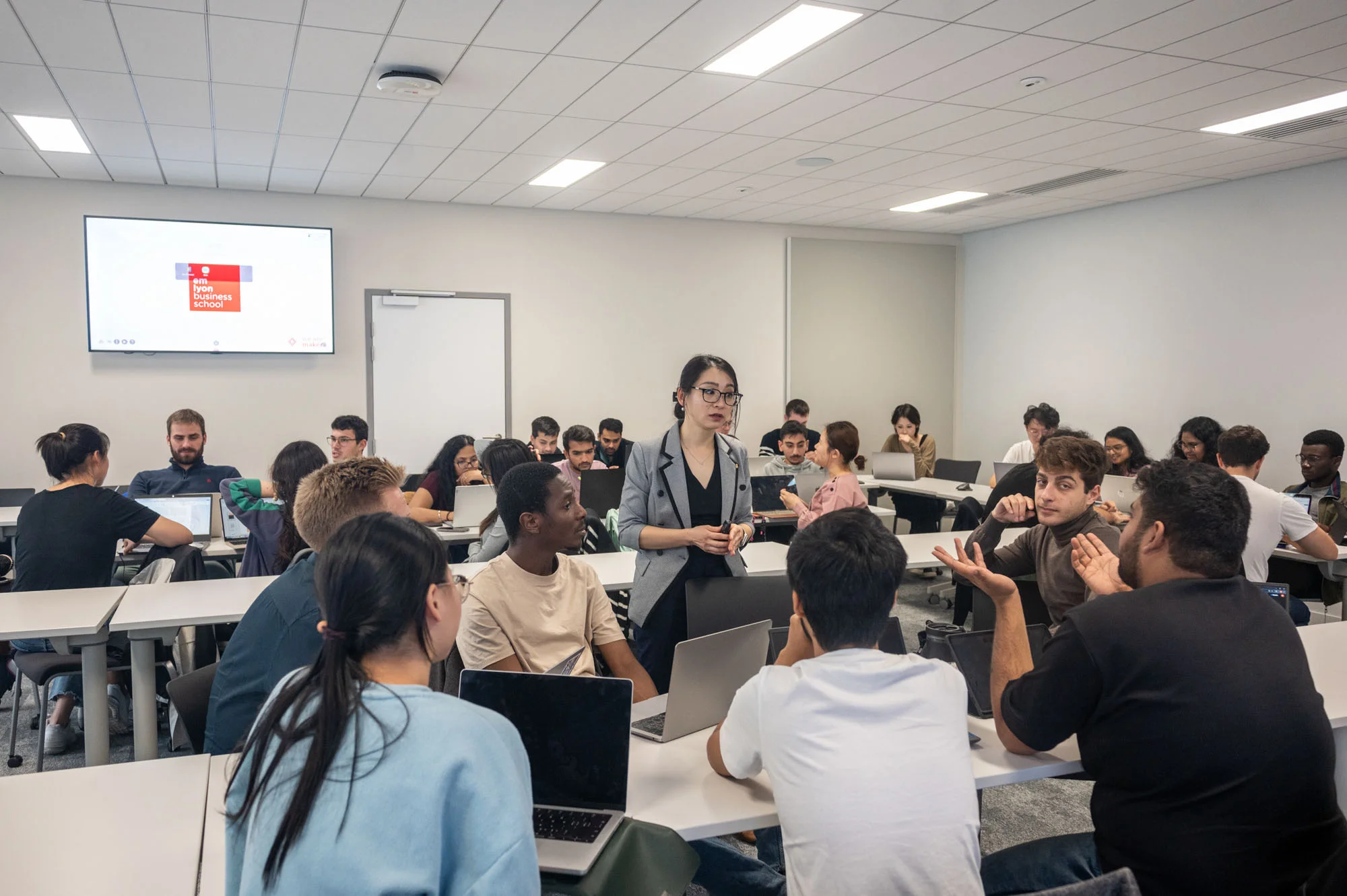 Group discussion taking place in emlyon classroom with students working on laptops