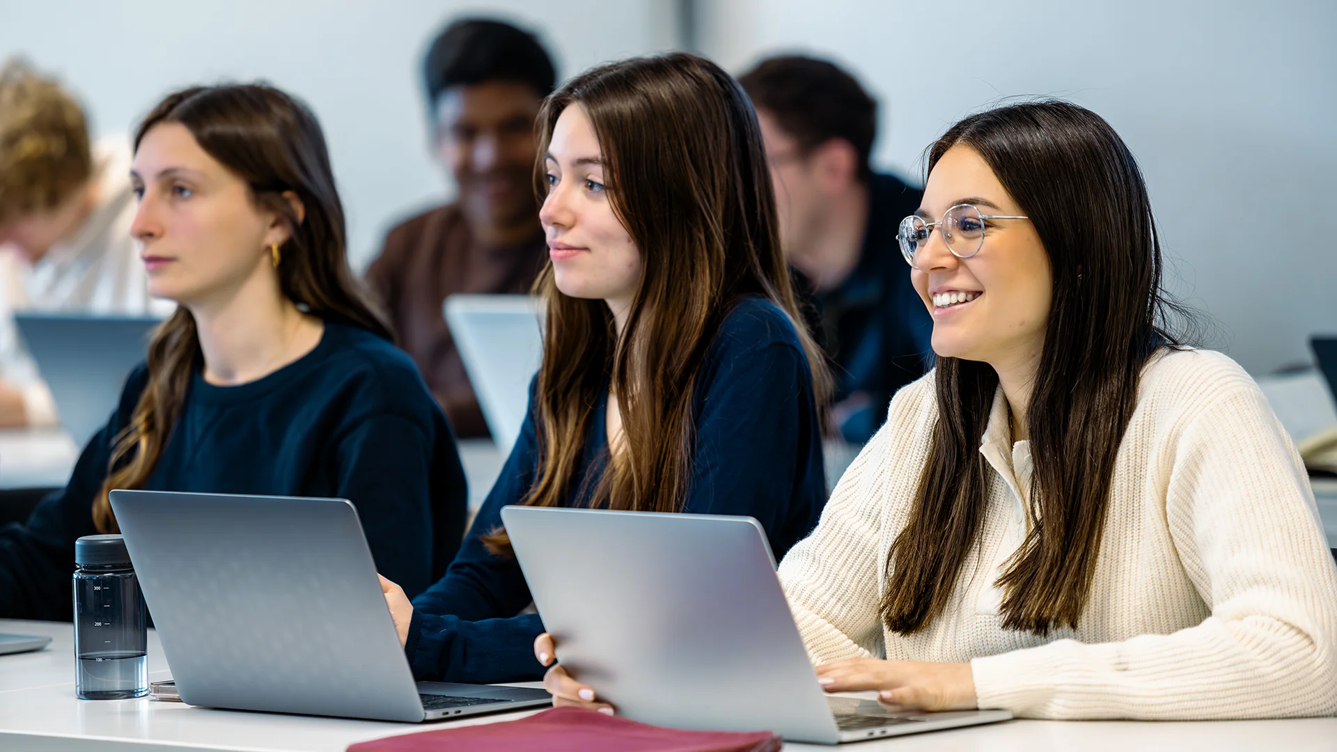 Students seated at desks using laptops during a class session in an emlyon classroom.