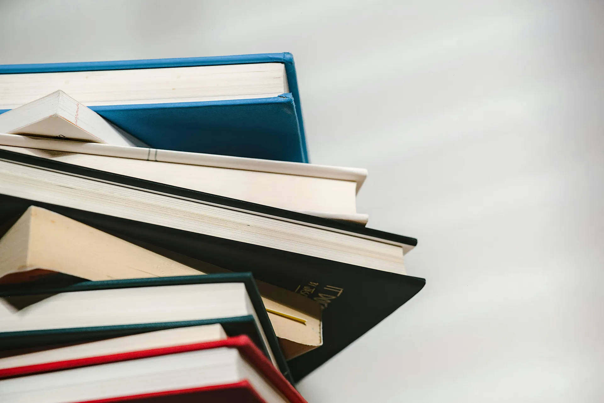 Pile de plusieurs livres reliés de différentes couleurs, empilés en biais, sur un fond clair.