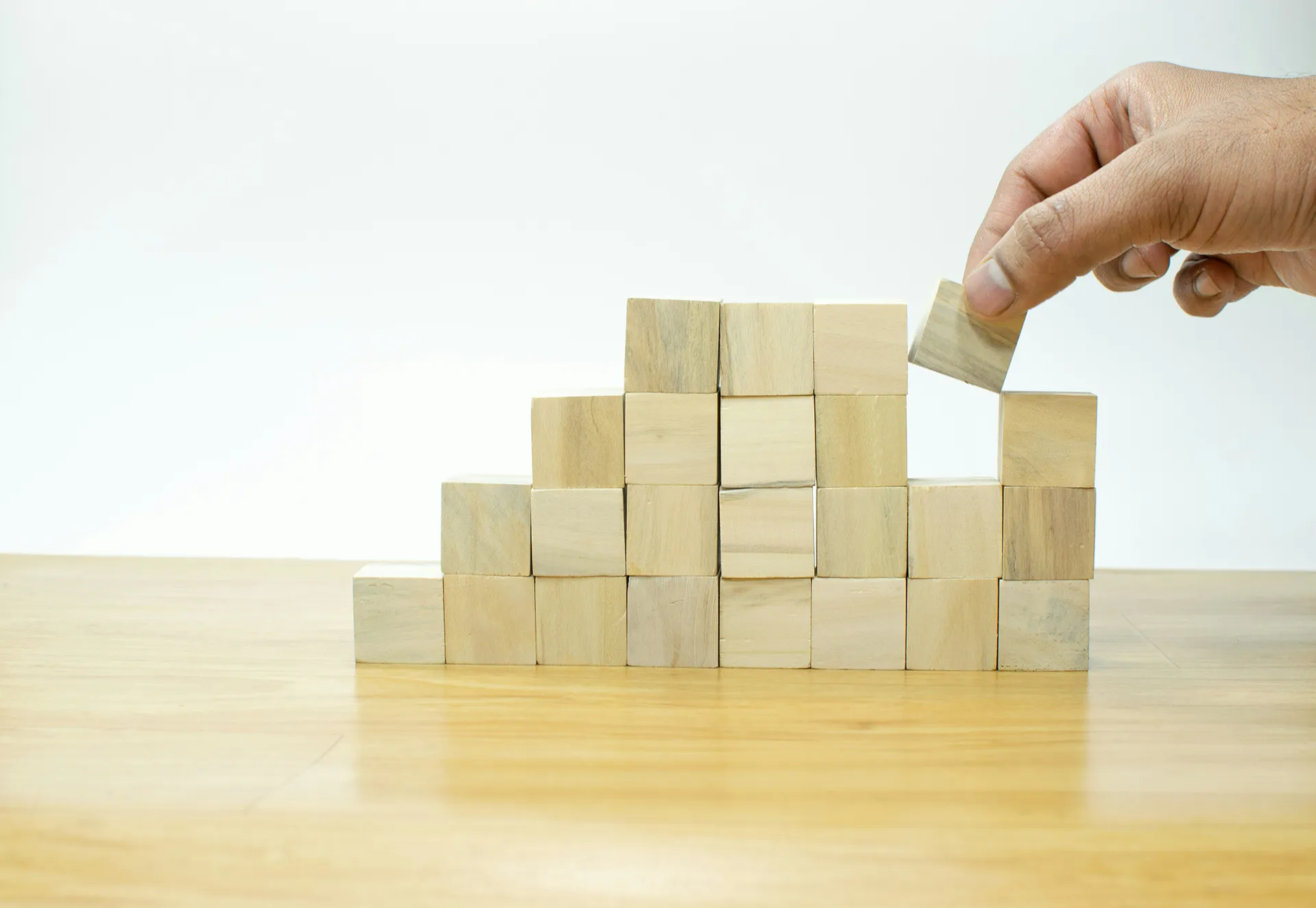 Main plaçant un bloc en bois au sommet d’une structure de cubes en bois disposés en escalier sur une table.