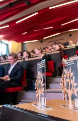 Awards displayed on a table during a ceremony in a lecture hall filled with attendees.