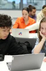 Étudiants travaillant ensemble sur un ordinateur portable dans une salle de classe moderne durant une session académique.