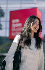 Group of students walking in front of the modern emlyon business school building, featuring glass architecture and a red sign in the background.