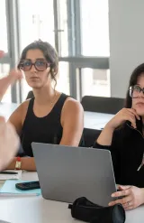 Personnes assises dans une salle de formation, écoutant une intervention et utilisant un ordinateur portable à une table.