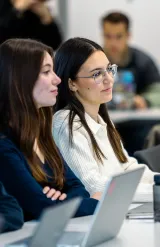 Students seated in a classroom using laptops during a university lecture.