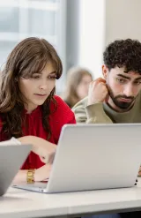 Étudiants en école de commerce travaillant en groupe sur ordinateurs portables en salle de cours.