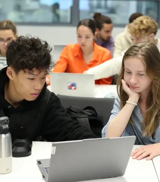 Étudiants travaillant ensemble sur un ordinateur portable dans une salle de classe moderne durant une session académique.