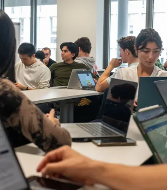 “IMBA students at emlyon working together in a bright classroom, seated around tables with laptops, engaged in discussion and collaborative work.