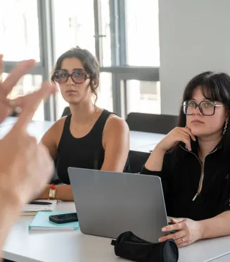 Personnes assises dans une salle de formation, écoutant une intervention et utilisant un ordinateur portable à une table.