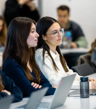 Students seated in a classroom using laptops during a university lecture.