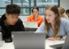 Students working on laptops in a classroom, with one person in focus in the center and others blurred in the foreground and background