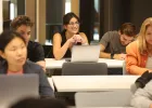 tudents using laptops in a classroom, with one person in focus at the center surrounded by classmates working at desks
