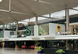 The image displays a vibrant area within Station F, showcasing various startup offices and collaborative spaces. Notable companies like Plug and Play and Mistral AI are represented, emphasizing the entrepreneurial spirit of the environment. The design is modern and dynamic, featuring colorful artwork that adds a creative touch to the workspace. This bustling hub reflects a commitment to fostering innovation and collaboration among startups and tech companies.