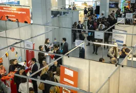 Overview of an indoor career fair with multiple booths and people interacting throughout the exhibition area.
