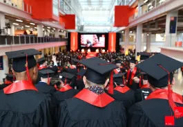 Graduates from emlyon business school wearing academic gowns and mortarboards, seen from behind during the graduation ceremony in the atrium.