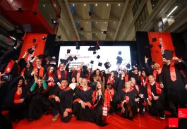 Group of emlyon business school graduates on stage throwing mortarboards during the graduation ceremony.