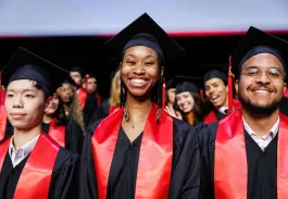 Groupe de diplômés en toge noire et écharpe rouge posant sur scène lors d’une cérémonie de remise de diplômes.