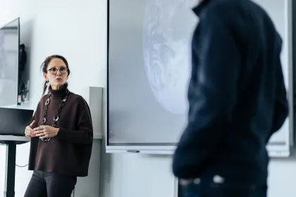 Two people talking and working in front of a large screen.