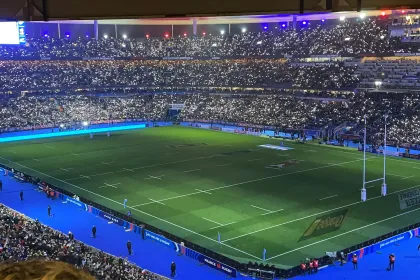 Vue du terrain de rugby avec des lumières scintillantes dans un stade rempli de supporters.