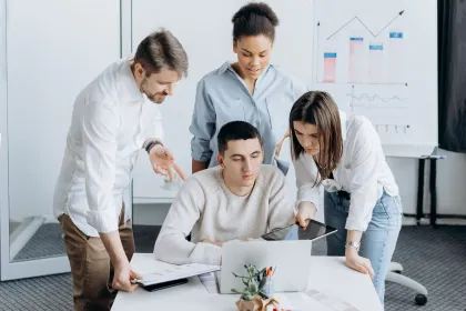 Groupe d’apprenants travaillant en équipe autour d’un ordinateur portable, analysant des documents et des graphiques dans une salle de formation.