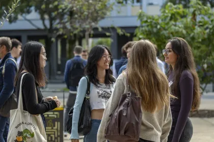 Group of emlyon students talking outdoors on campus, surrounded by other people and trees.