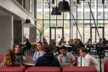 Étudiants d’emlyon business school travaillant et échangeant dans un espace commun du campus, avec vue sur l’atrium et les tables de travail.