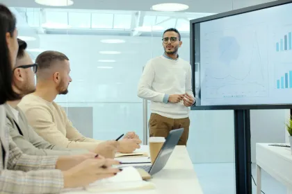 Présentation professionnelle avec un intervenant expliquant des graphiques de performance à une équipe en réunion dans une salle de conférence moderne.