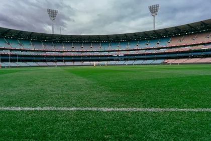 Vue panoramique d’un grand stade vide avec pelouse verte, gradins circulaires et éclairage de match sous un ciel nuageux.