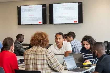 Groupe d’étudiantes et étudiants d'emlyon business school collaborant en classe devant des écrans affichant une présentation pédagogique.