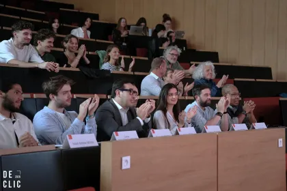 Public assis dans un amphithéâtre universitaire, applaudissant après une présentation ou une conférence.