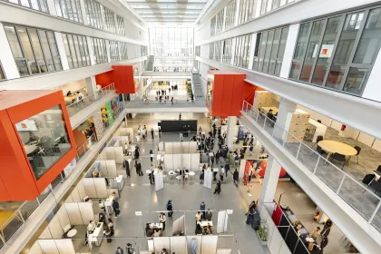Atrium lumineux d’un campus avec espaces de travail, stands et visiteurs répartis sur plusieurs niveaux