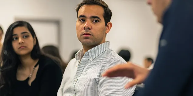 Un groupe de personnes attentives lors d'une discussion interactive, avec une personne au centre portant une chemise à rayures, écoutant attentivement.