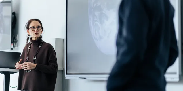 Two people talking and working in front of a large screen.