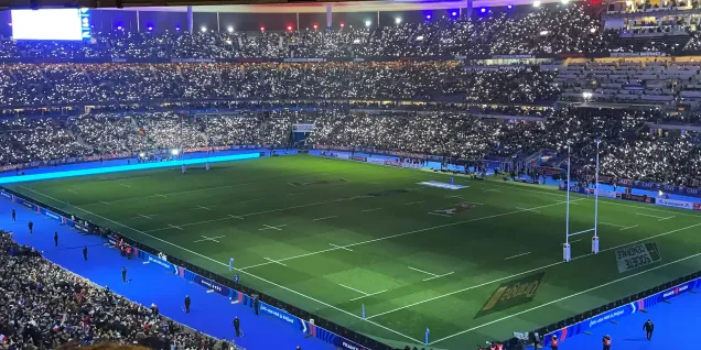 Vue du terrain de rugby avec des lumières scintillantes dans un stade rempli de supporters.