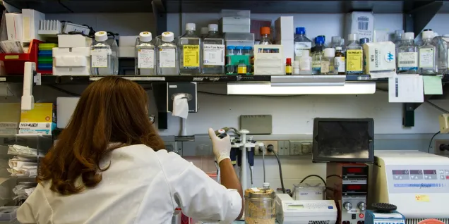 Research worker in a fully equipped laboratory handling scientific instruments on a bench filled with equipment, reagents and lab materials.